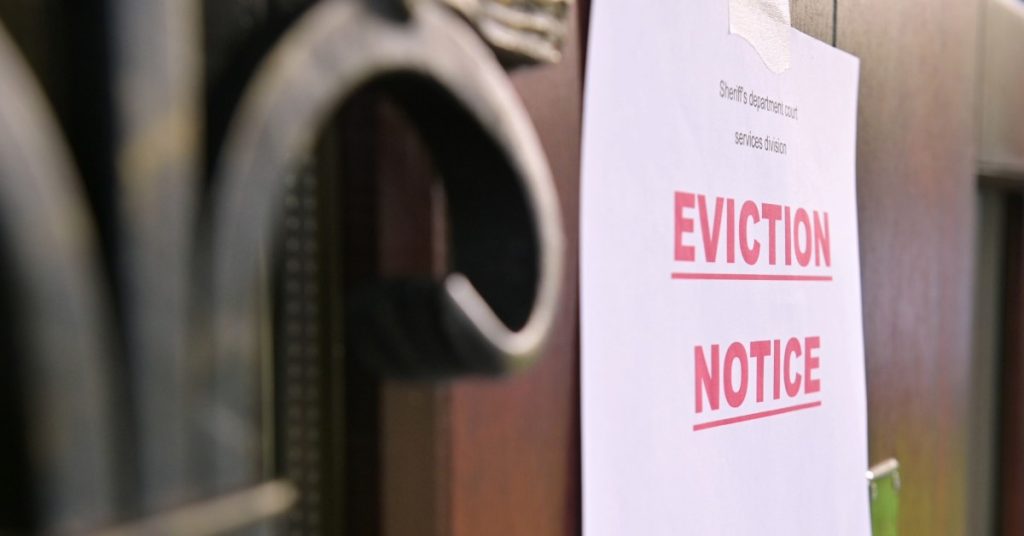 A close-up of a piece of paper with giant, bold letters that read "EVICTION NOTICE" taped to the front of a brown door.