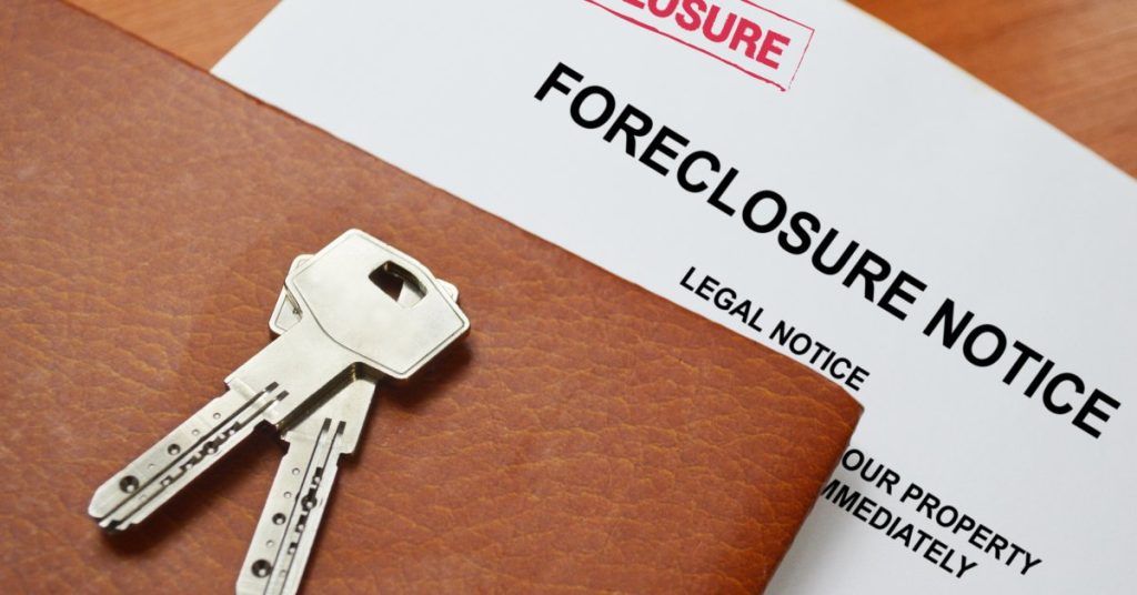 A close-up of a pair of house keys on a leather folder over a white document that reads, "FORECLOSURE NOTICE."