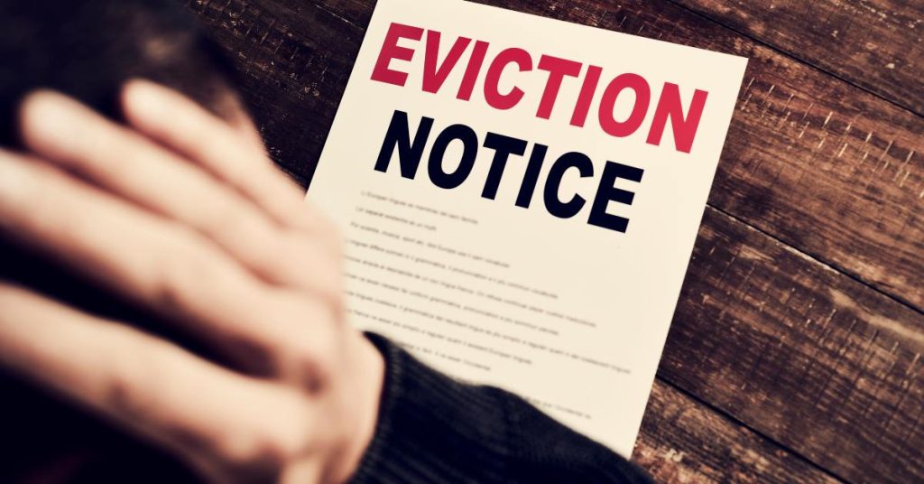 An over-the-shoulder view of a man looking at a piece of paper that reads "EVICTION NOTICE" on a wooden table.