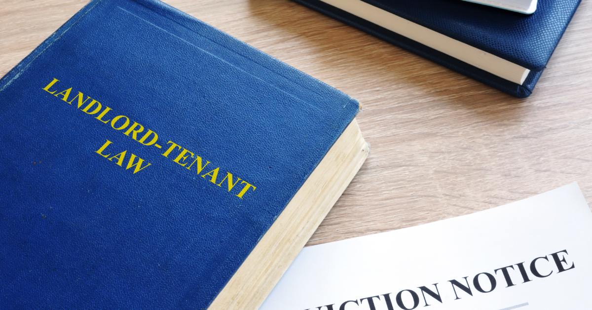 A blue, leather-bound book with the title "Landlord-Tenant Law" next to a white eviction notice on a wood desk.