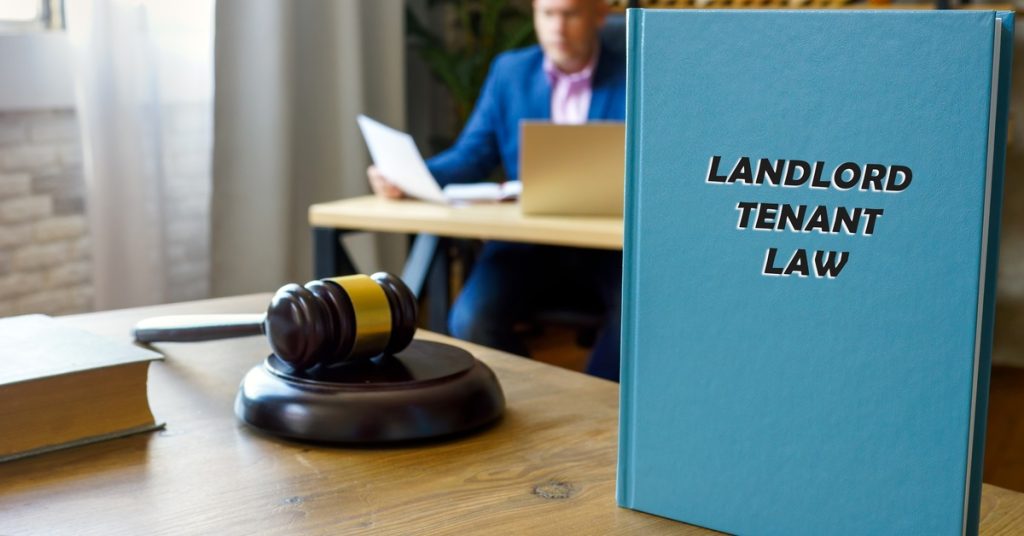 A blue book with the title "LANDLORD TENANT LAW" standing vertically on a table next to a courtroom gavel and book.